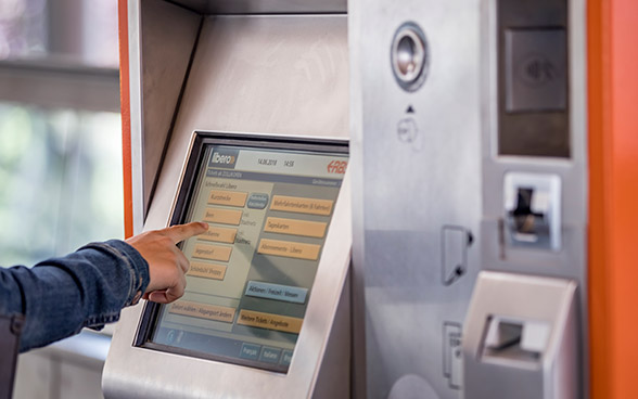 Ein Billettautomat mit Touch-Screen, im Vordergrund eine Hand.